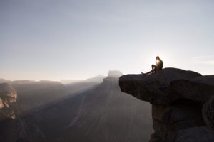 A person sits at the top of a high cliff at sunrise